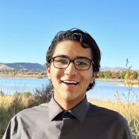 Person in glasses smiling in front of field and lake